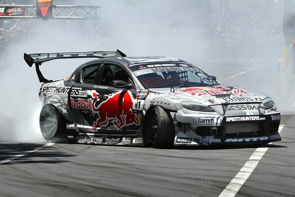 Auf der Strecke driftet ein sportlicher Mazda mit Werbung für ein Red-Bull-Getränk