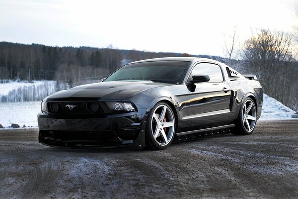 Ford Mustang nera sulla strada vicino alla foresta innevata