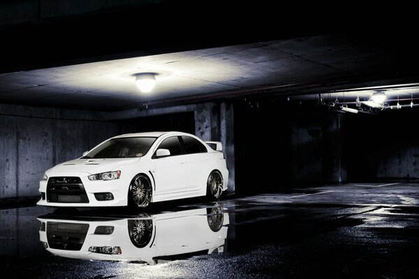 A white Mitsubishi evolution under a lantern with a reflection in a puddle