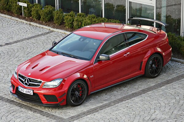 Mercedes rouge C63 à côté d un immeuble de luxe