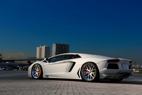 Schneeweißer Lamborghini vor dem Hintergrund von hohen Gebäuden aus blauem Himmel