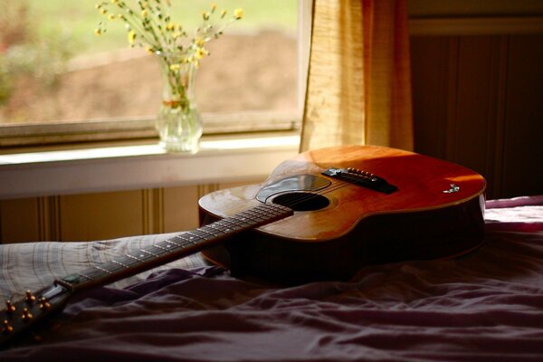 Guitare sur berceau et vase avec des fleurs sur la fenêtre