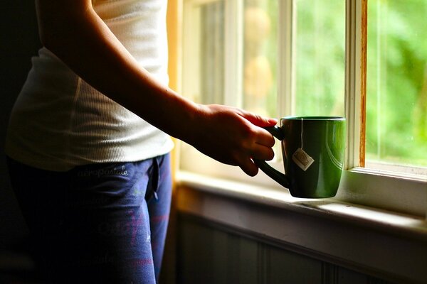 Una taza de té verde en las manos de la ventana