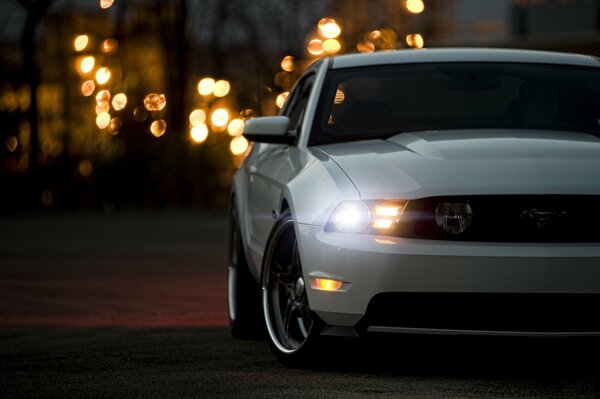 A white Ford Mustang is driving on the road in the evening