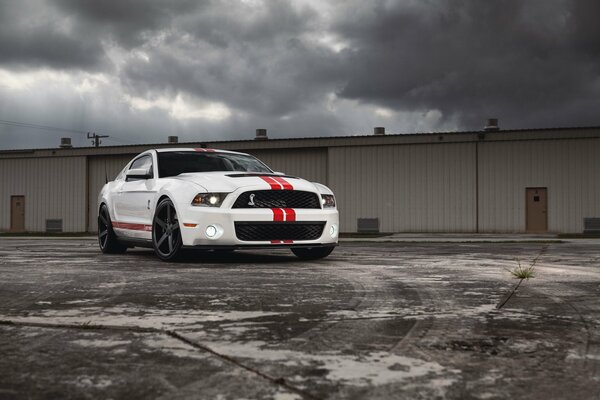 Una Mustang bianca con strisce rosse si trova di fronte ai garage