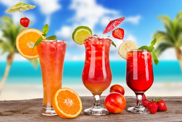 Three fruit cocktails with ice on the background of palm trees and the sky