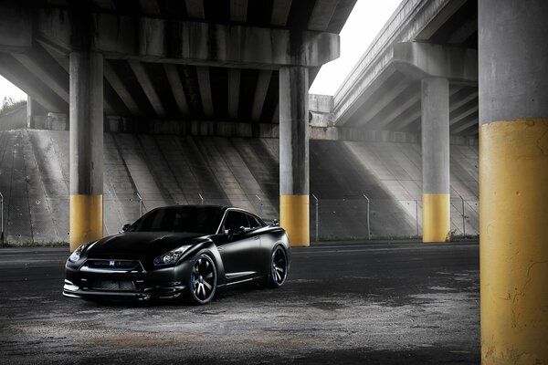 Black Nissan under the pillars of the bridge