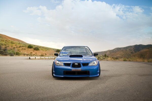 Subaru Impreza bleu sur une route en béton sur fond de collines