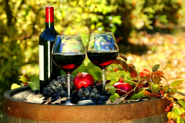 A pin and wine in glasses, bunches of grapes on a barrel