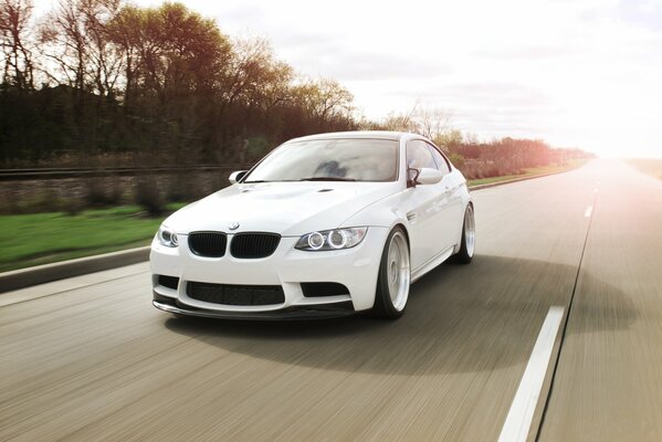 A white car is driving at speed on the road