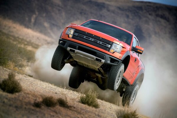 The Ford f-150 SUV rushes through the mountains among the grass raising dust