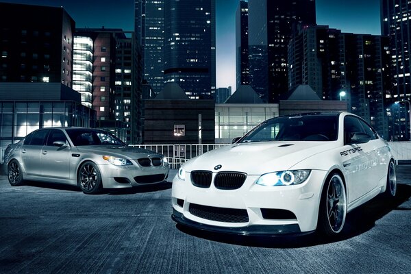 Two BMWs grey and white. Series 5 and 3 stand against the background of the city