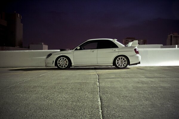 White Subaru impreza in an open parking lot, side view