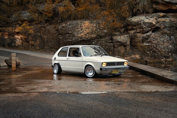 A white Volkswagen golf stands on the rise by the stream