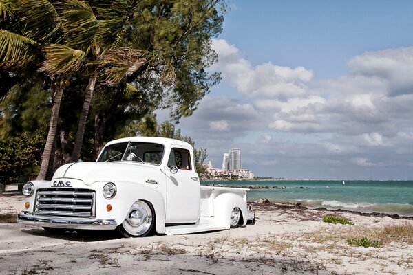 Camioneta GMC retro blanca con fondo de playa y palmeras