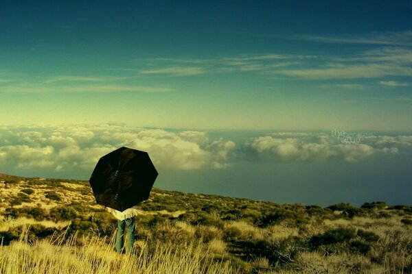 A man with an umbrella stands above the clouds on the mountain