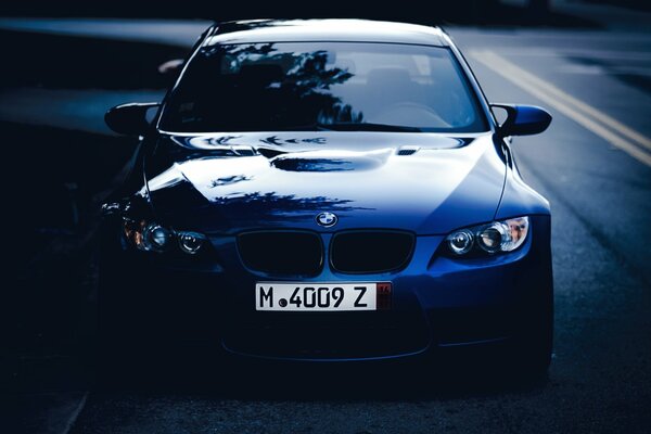 Une BMW M3 bleue garée sur une route ouverte sur un fond de ciel nocturne