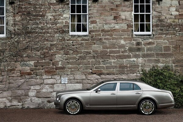 Silver Bentley on the background of the stone wall of the house