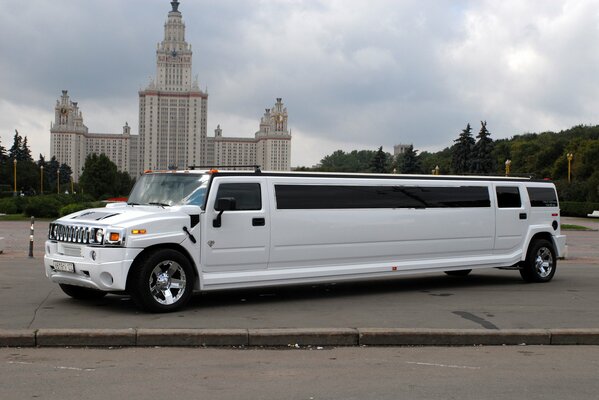 A white hummer limousine on the street in front of a large building