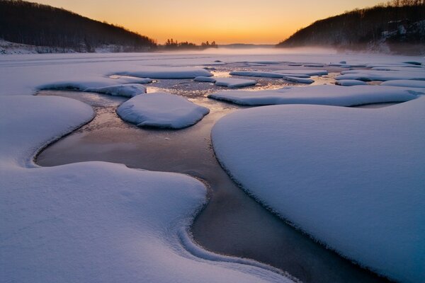 Ein Bach, der bei Sonnenuntergang von Schnee umgeben ist