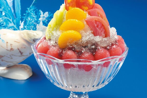 Postre de frutas en un tazón transparente sobre una pierna sobre un fondo azul