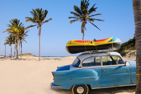 Auto blu Sovietica con barca sul tetto sulla spiaggia sabbiosa dell oceano sotto le palme sullo sfondo del cielo blu