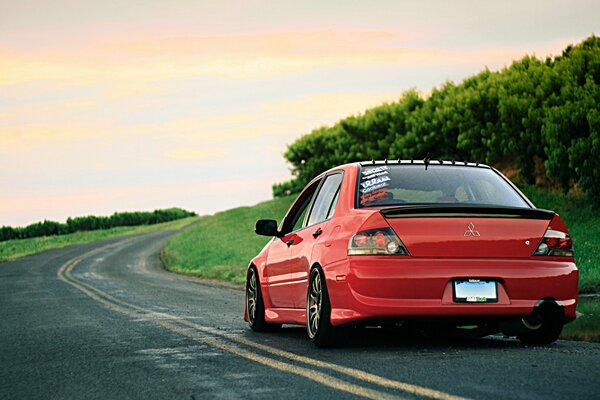 Mitsubishi lancer Red rast entlang der Straße zwischen Feldern und Bäumen