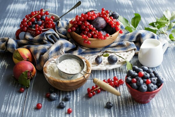 Manzanas, arándanos y grosellas en la mesa con harina y leche