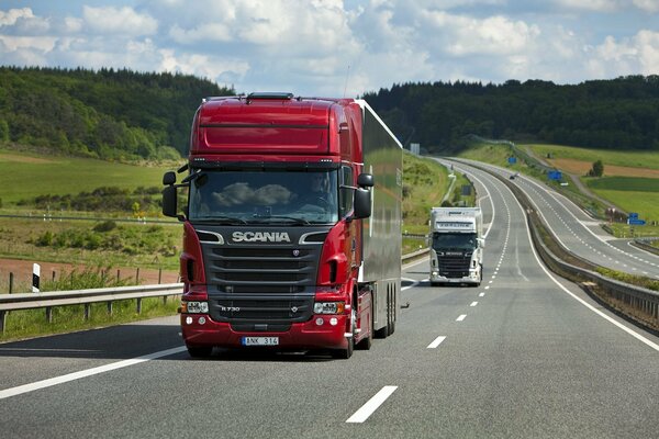 Un camión Scania rojo conduce por la carretera. Paisaje de verano con campos