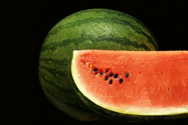 A sweating watermelon on a black background with a cut piece