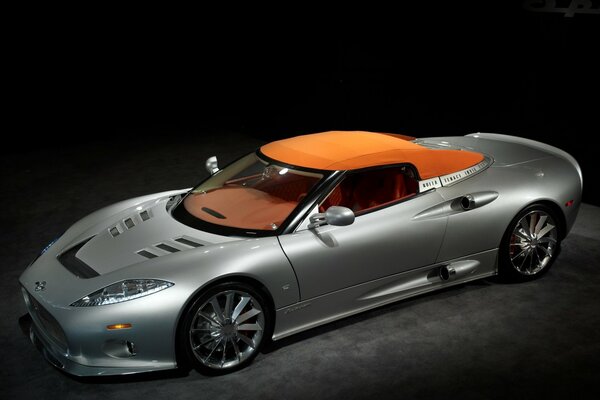 A silver car with an orange top on a dark background