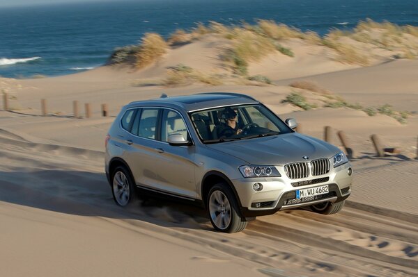 Silver bmw x3 rides on the sand against the background of the sea