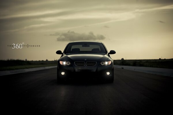 BMW with headlights on against the sky