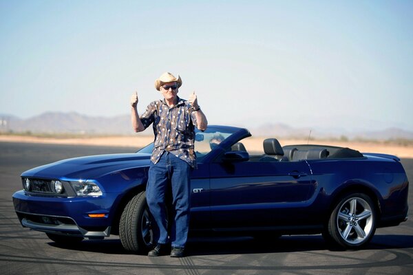 Homme debout près de Ford Mustang cabriolet bleu