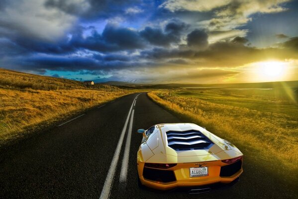 A yellow Lamborghini is driving on the highway. Around the landscape with fields at sunset