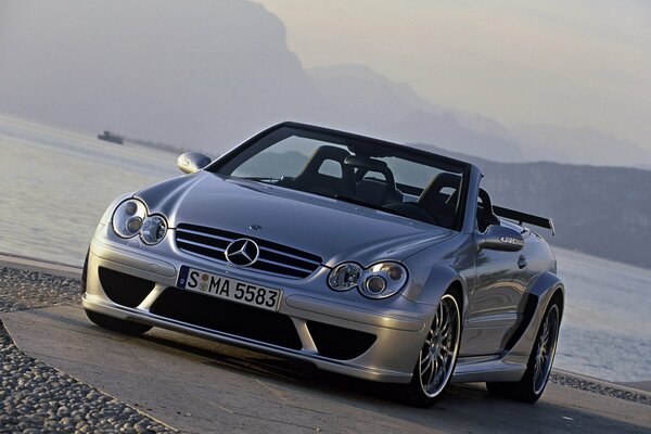 Mercedes silver-colored car on the background of water and road