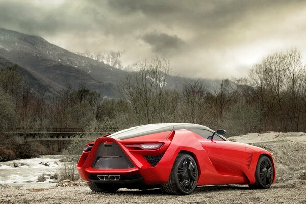 Un coche rojo inusual se encuentra fuera de la ciudad en el fondo de las montañas