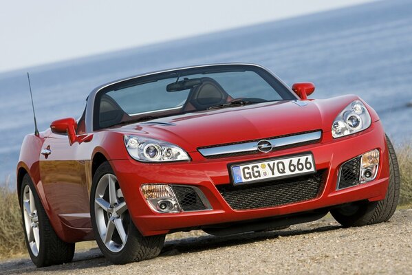 Red Opel convertible on the shore near the water surface