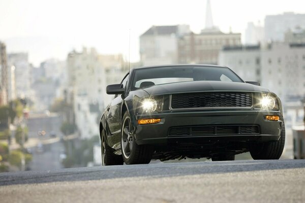 Ford Mustang bullitt ściga się po drodze na tle miejskich wieżowców