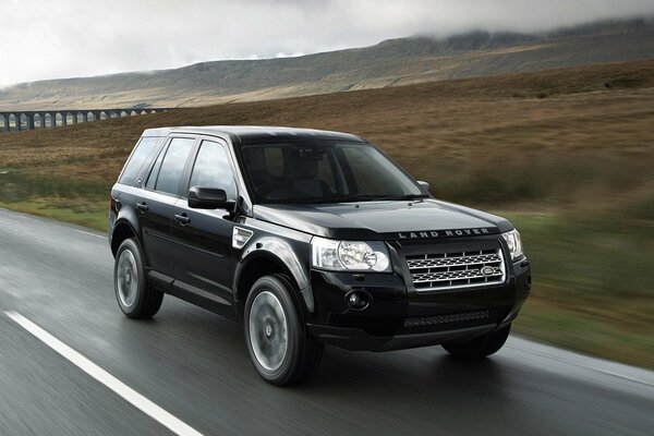 Black land rover rides on a country highway against the background of hills