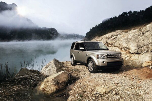 Range rover car is in the mountains on the slope of fog and river