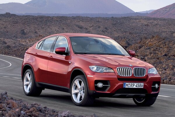 Red BMW car on the road in a rocky area against the background of mountains