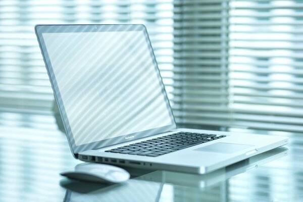 Laptop und Maus auf einem Tisch vor einem Fensterhintergrund