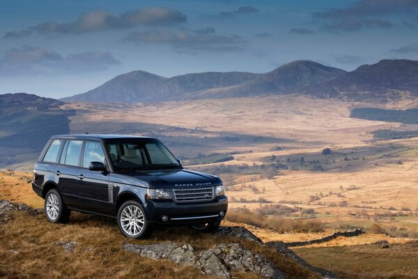 Una Range Rover nera si erge su una scogliera pesante sullo sfondo di una bellissima valle