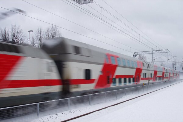 A double-decker train rushes at high speed in winter