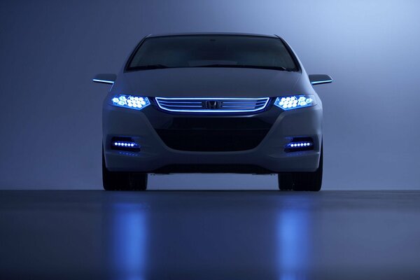 Honda con los faros encendidos sobre un fondo azul