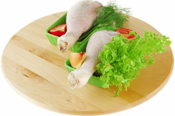 Deux cuisses de poulet dans des plateaux avec des légumes sur une planche ronde