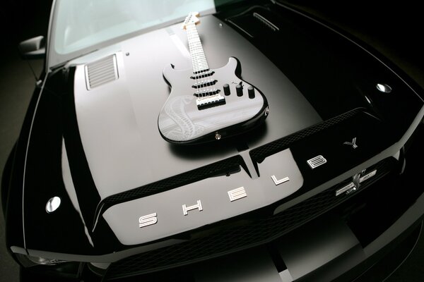 A Fender stratocaster guitar is lying on the hood of a black car