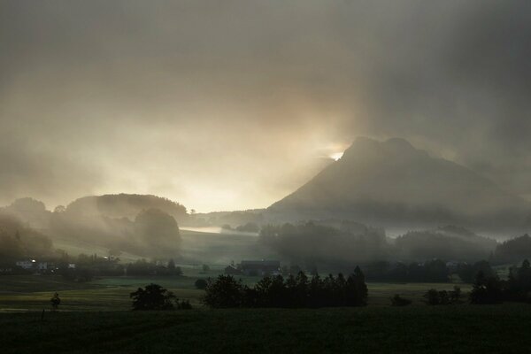 Nebel in den Bergen über Häusern und Bäumen. Nebliger Himmel über einer Bergsiedlung und Bäumen