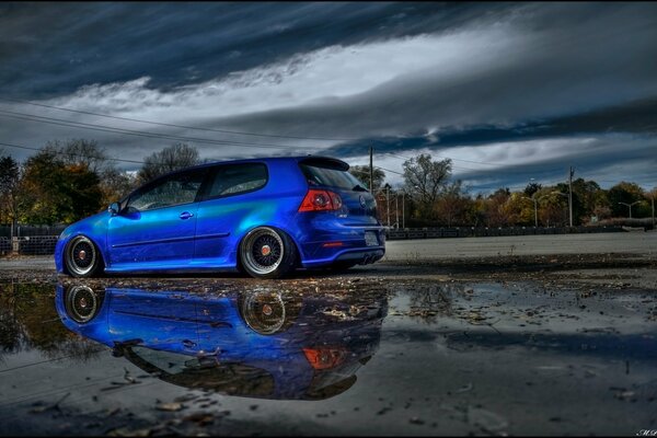 Voiture Volkswagen golf bleu sur fond de route mouillée